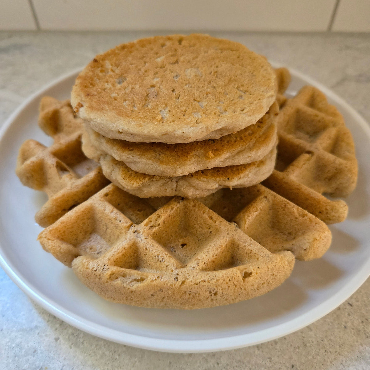 3 pancakes and 1 waffle stacked on a white plate.