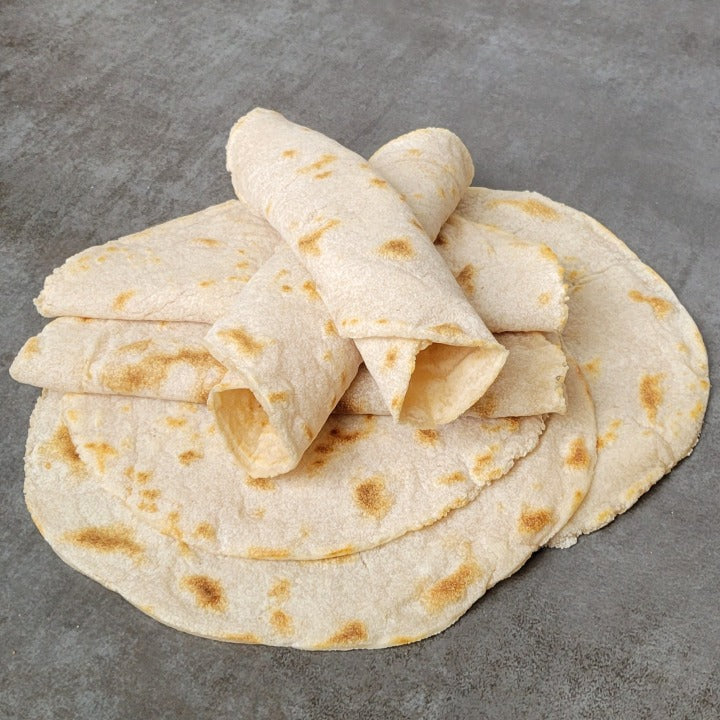A stack of original tortillas. Some rolled up, some folded in half on a grey background.