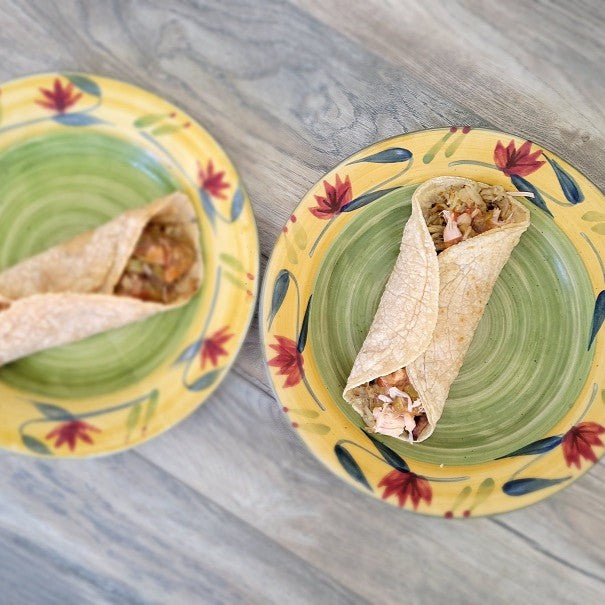 2 breakfast burritos on 2 plates. the plates have a yellow band with red flowers and green leaves. the center of the plate is green.
