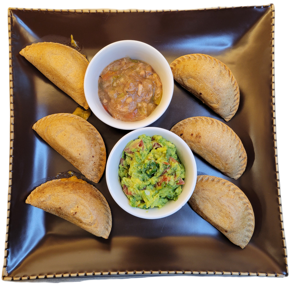 A brown plate with 6 empanadas, 1 white bowl of green chile, and a white bowl of guacamole.
