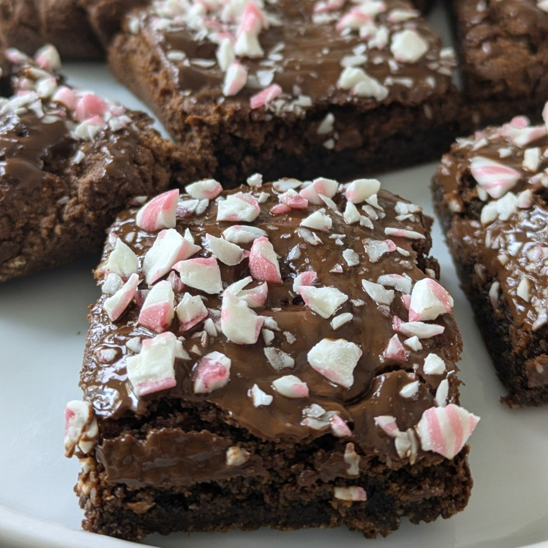 Frosted brownies with crushed candy canes sprinkled on top on a white plate.