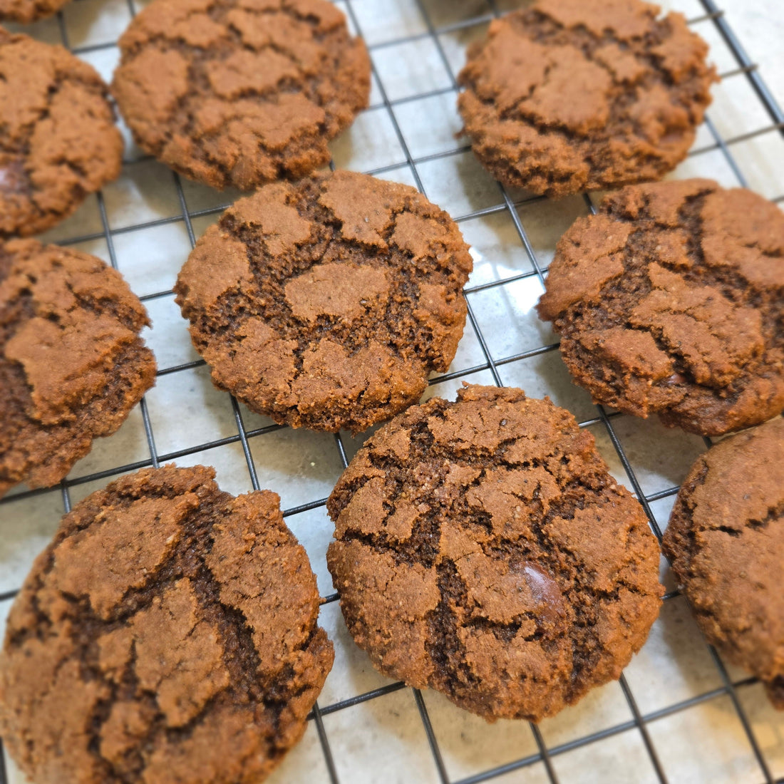 9 Cassavaberry Carob Cookies cooling on a cooling rack on a white counter.