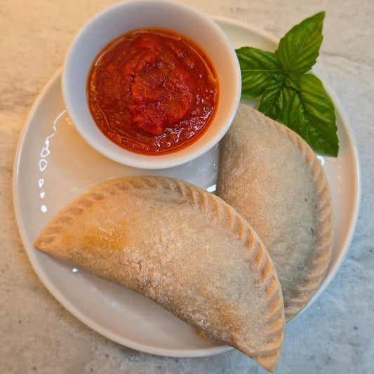 Two Gluten Free Cassavaberry calzones with a cup of marinara sauce and sprig of basil on a white plate.