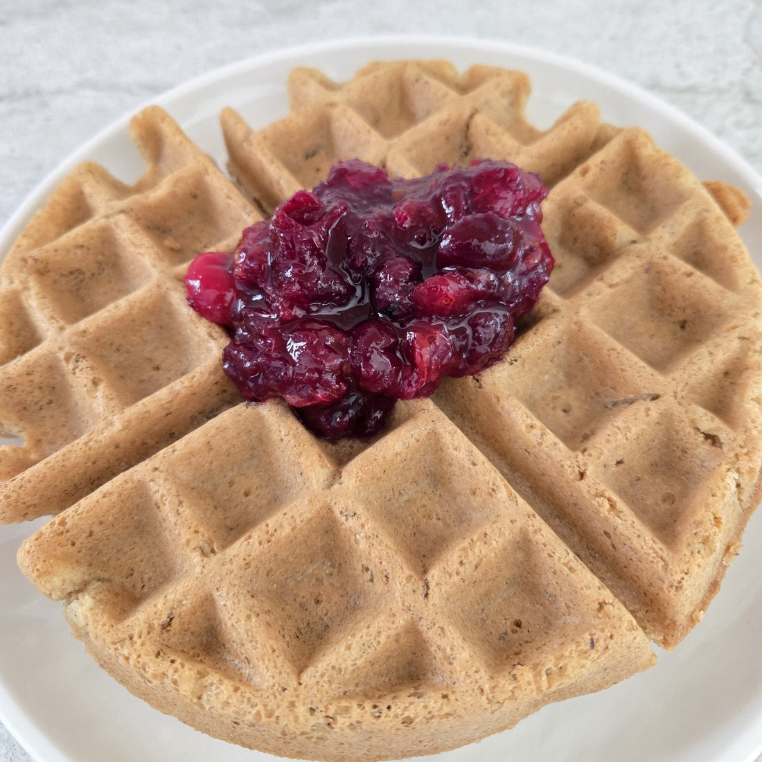 Waffle with fruit sauce on the top on a white plate.