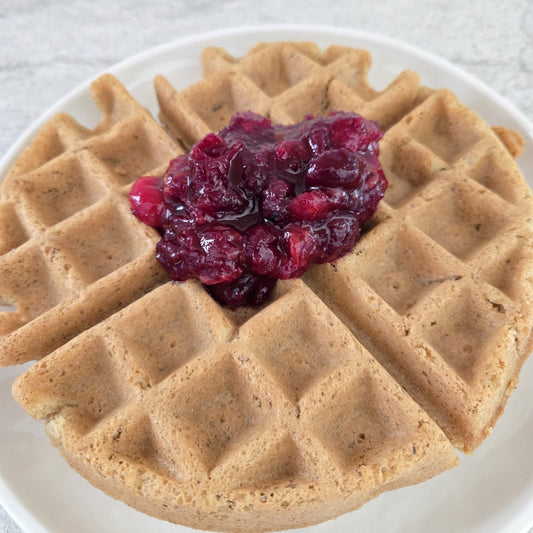 Waffle with fruit sauce on the top on a white plate.