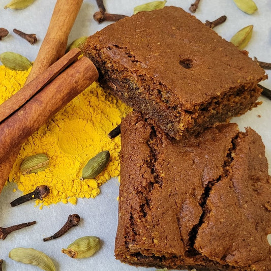 Almond flour pumpkin spice brownies cut into squares and stacked with pumpkin powder, cinnamon sticks, cardamon pods, cloves around the brownies
