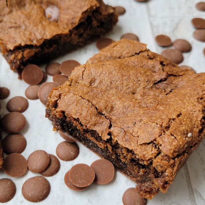 Baked carob brownies with carob chips sprinkled around the brownies on a white background.