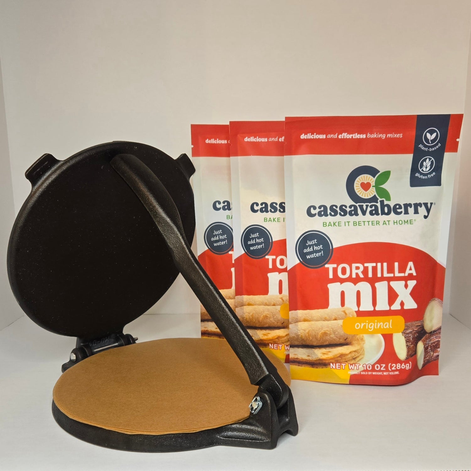 Black tortilla press and 3 Cassavaberry gluten-free and grain-free tortilla mix packages on a white background.