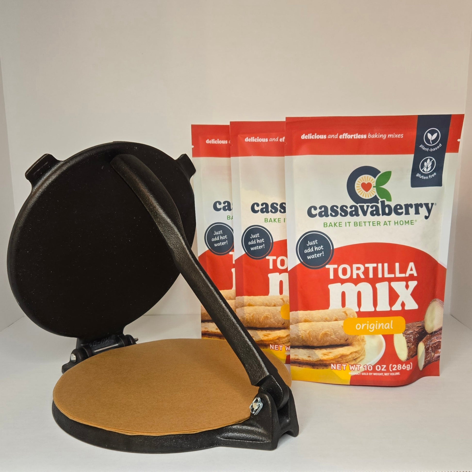 Black tortilla press and 3 Cassavaberry gluten-free and grain-free tortilla mix packages on a white background.