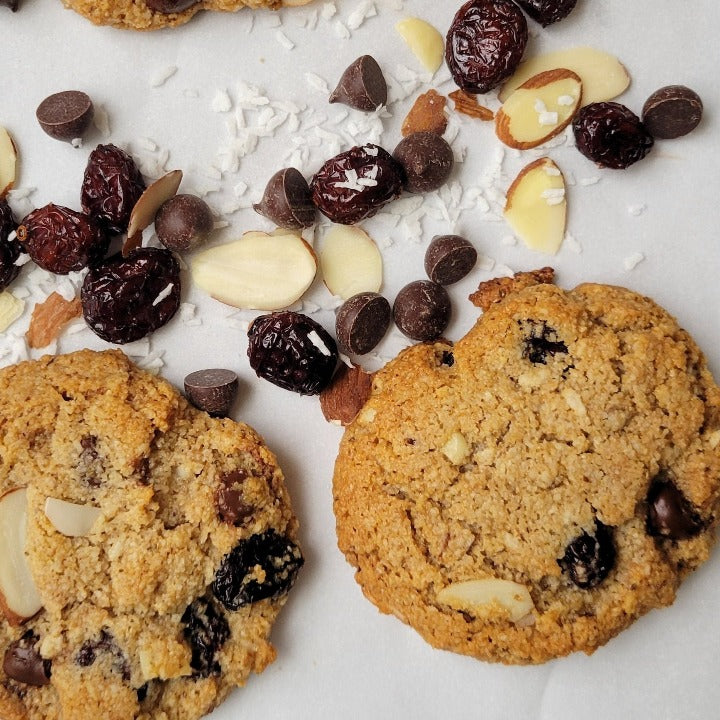 Loaded cookies shown with coconut, chocolate chips, sliced almonds and dried cranberries on a white background.