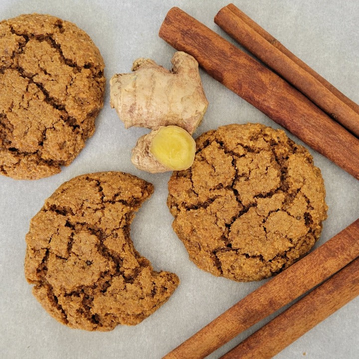 Group of 3 Gingersnap cookies with cinnamon sticks and 2 pieces of ginger around the cookies.