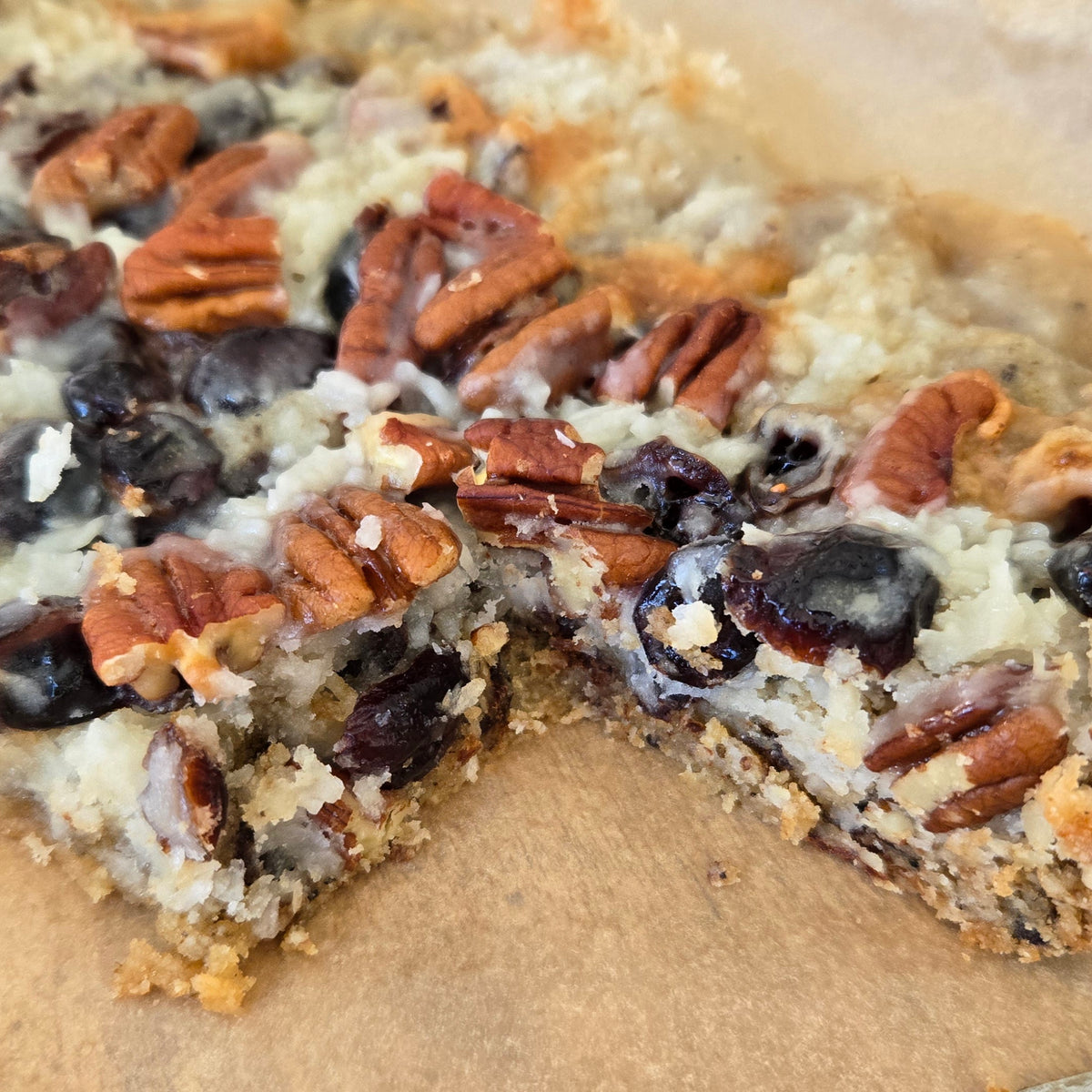 Close-up of a Magic Bars dessert with pecans and cranberries and coconut on a wooden board.