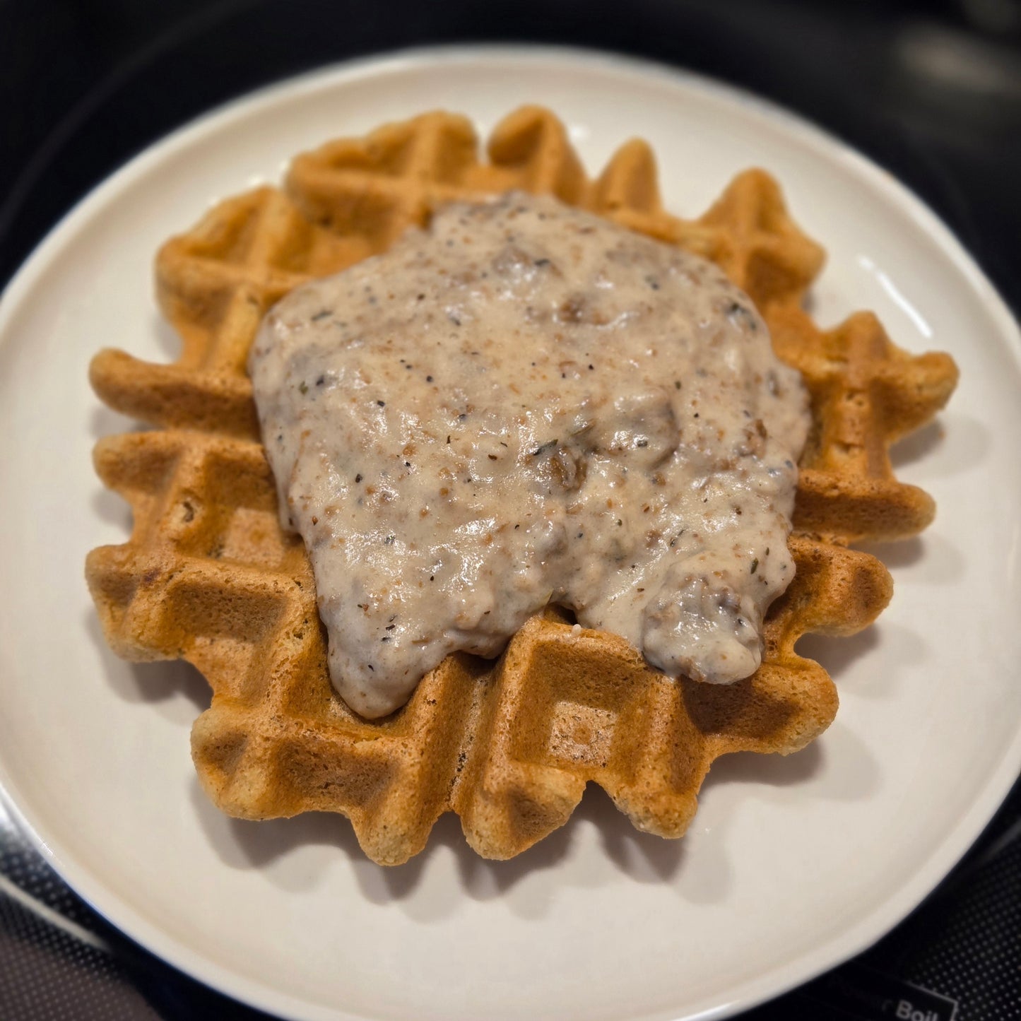 Our gluten free, vegan waffle on a white plate topped with vegan sausage gravy.