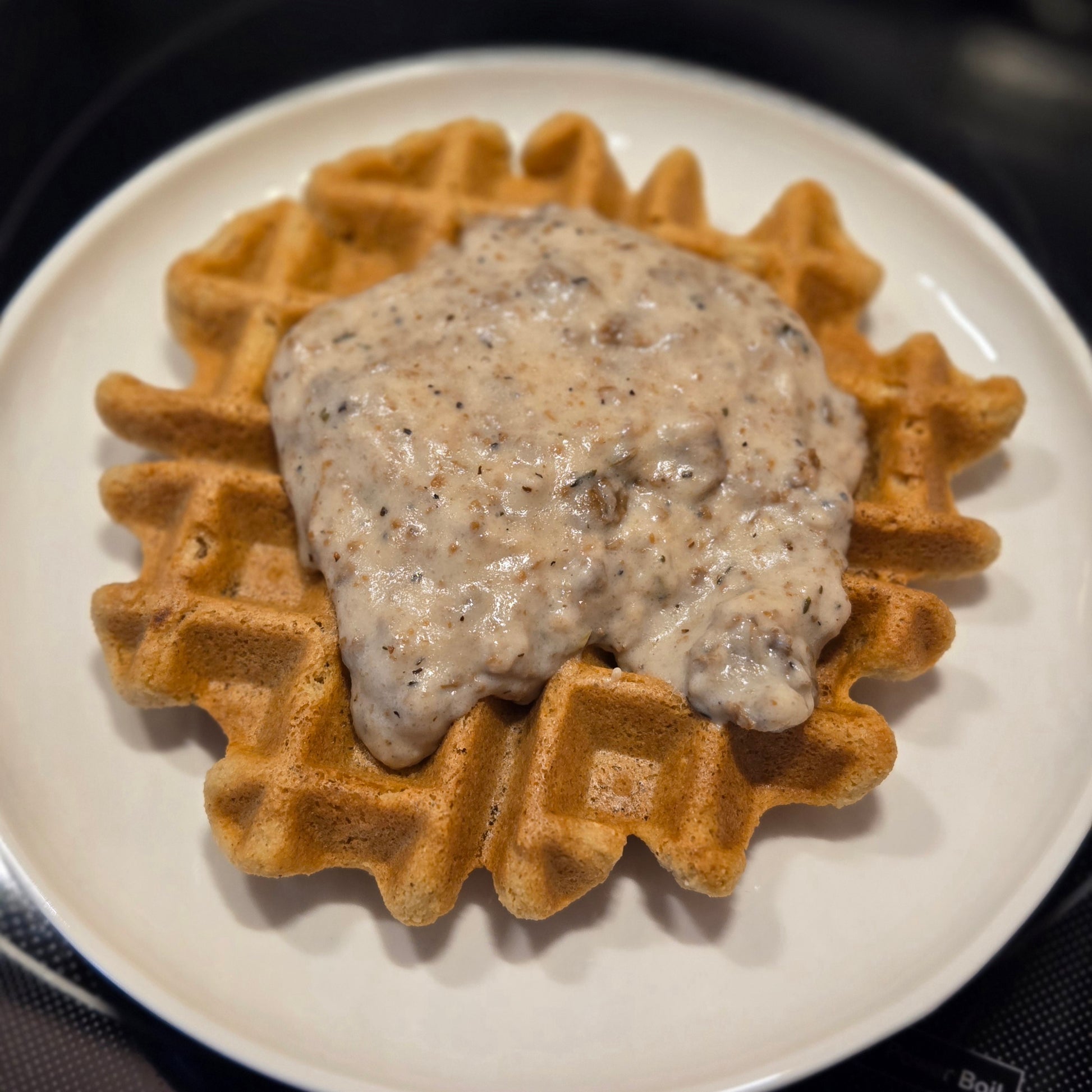 Our gluten free, vegan waffle on a white plate topped with vegan sausage gravy.