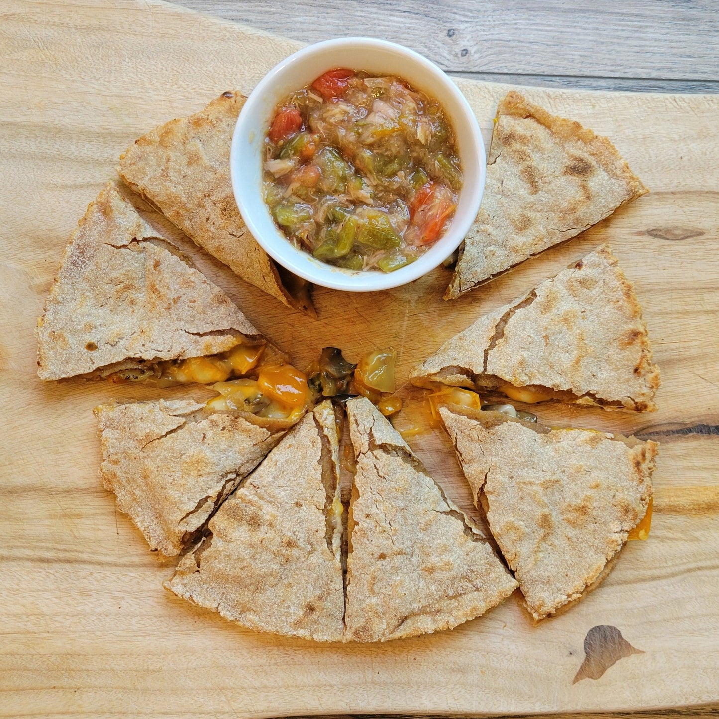 Quesadillas cut into triangles on a wooden cutting board with a side of green chile.
